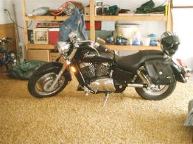 1989 Ford Bronco - A black motorcycle is parked in a garage or workshop, with shelves and storage in the background. The SuperMotors.net logo is visible on th…