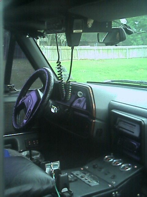 1989 Ford Bronco - Interior view across a truck cab from the passenger side, showing a wrapped steering wheel, wood-grain dash trim, an overhead-mounted CB ra…