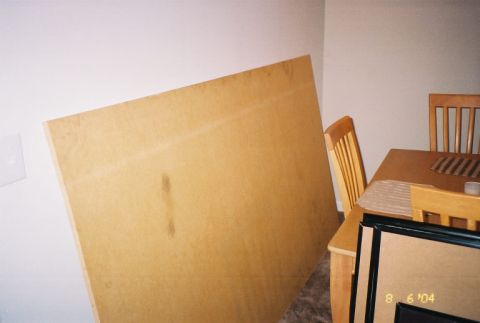 1988 Ford Bronco - A large piece of particle board is propped against a wall in a room with a dining table and chairs.