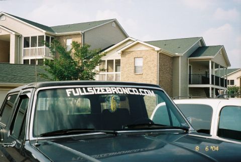 1988 Ford Bronco - A dark gray Ford Bronco is parked in front of apartment buildings, with a white SUV beside it.