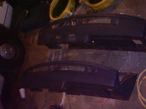 1991 Ford LTD Crown Victoria - Two bare dark-gray dashboard assemblies pulled from a car lie side by side on a garage floor, stripped of gauges, vents and trim so the ins…