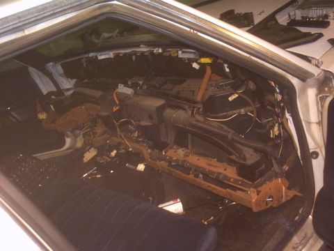 1991 Ford LTD Crown Victoria - Interior of a white sedan photographed through the open passenger door with the dashboard completely removed, exposing the bare steel dash…