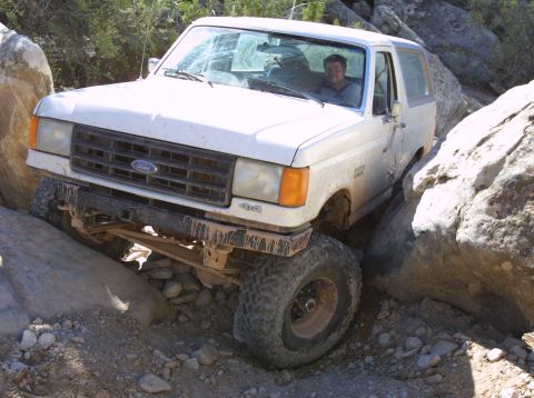 1987 Ford Bronco - A white 1987 Ford Bronco is shown maneuvering through a challenging rocky terrain.