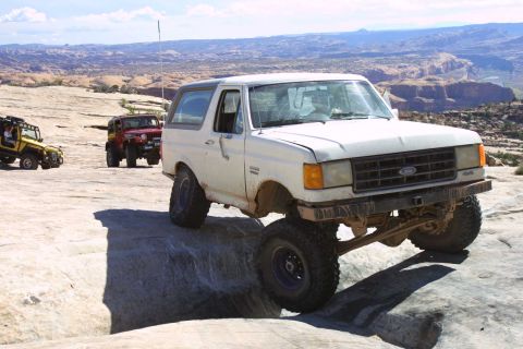 1987 Ford Bronco - A white 1987 Ford Bronco navigates a rocky trail with other off-road vehicles in the background.