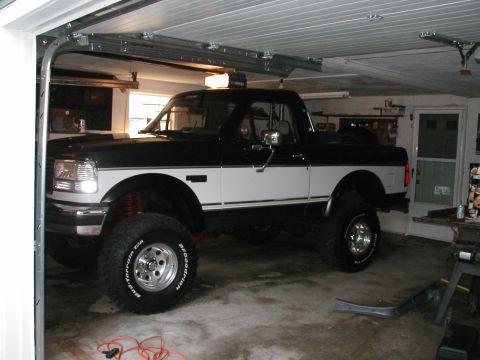 1994 Ford Bronco - This two-tone pickup truck is parked inside a garage with the door partially open.