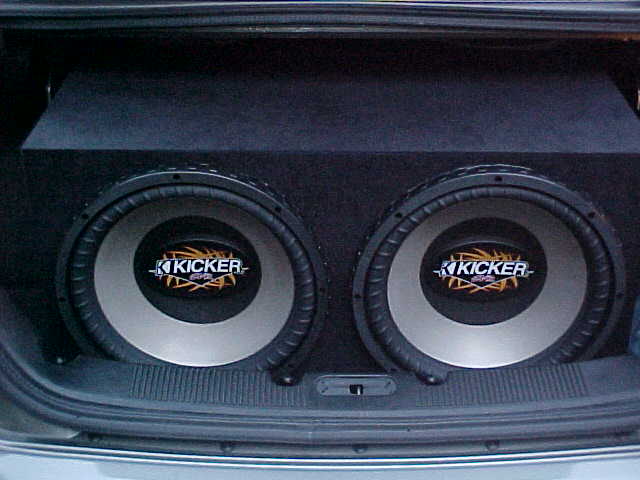 Two Kicker subwoofers in a black carpeted box mounted in a car trunk