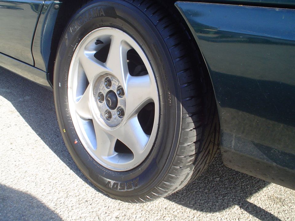 Close-up of a silver five-spoke alloy wheel on a dark green car