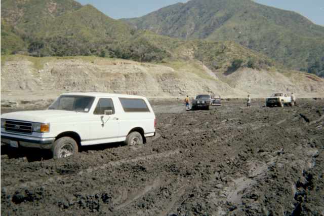 White full-size Ford Bronco parked in a churned muddy field with mountains