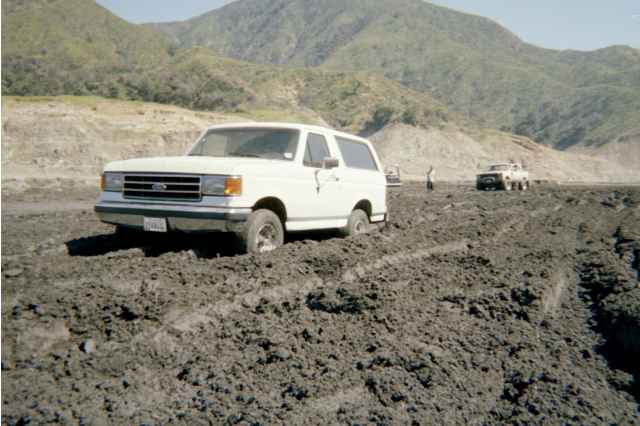 White full-size Ford Bronco in a muddy off-road field, front three-quarter