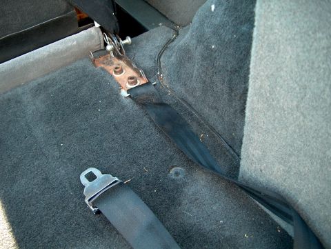 1994 Ford Bronco - The interior of a vehicle shows a black seatbelt and its metal buckle attached to the floor.