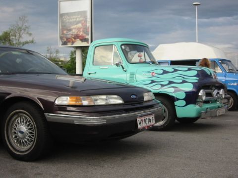 1992 Ford Crown Victoria - A row of vehicles, including a dark sedan and a custom pickup truck with flame graphics, are parked outdoors.