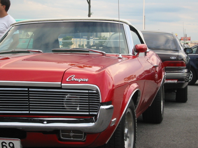 Red convertible with 'Cougar' script on fender, parked next to a black sedan