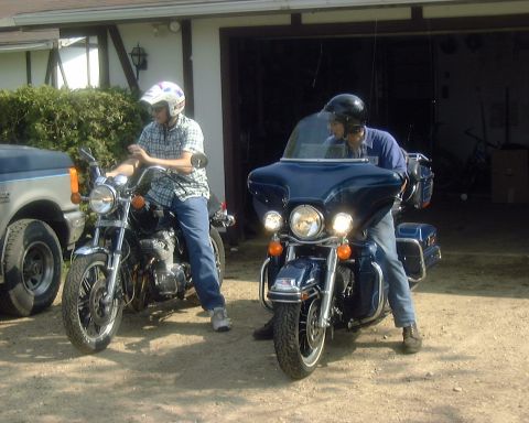 1985 Ford F-150 - Two motorcyclists prepare to ride in front of a suburban garage, with a Ford truck partially visible on the left.