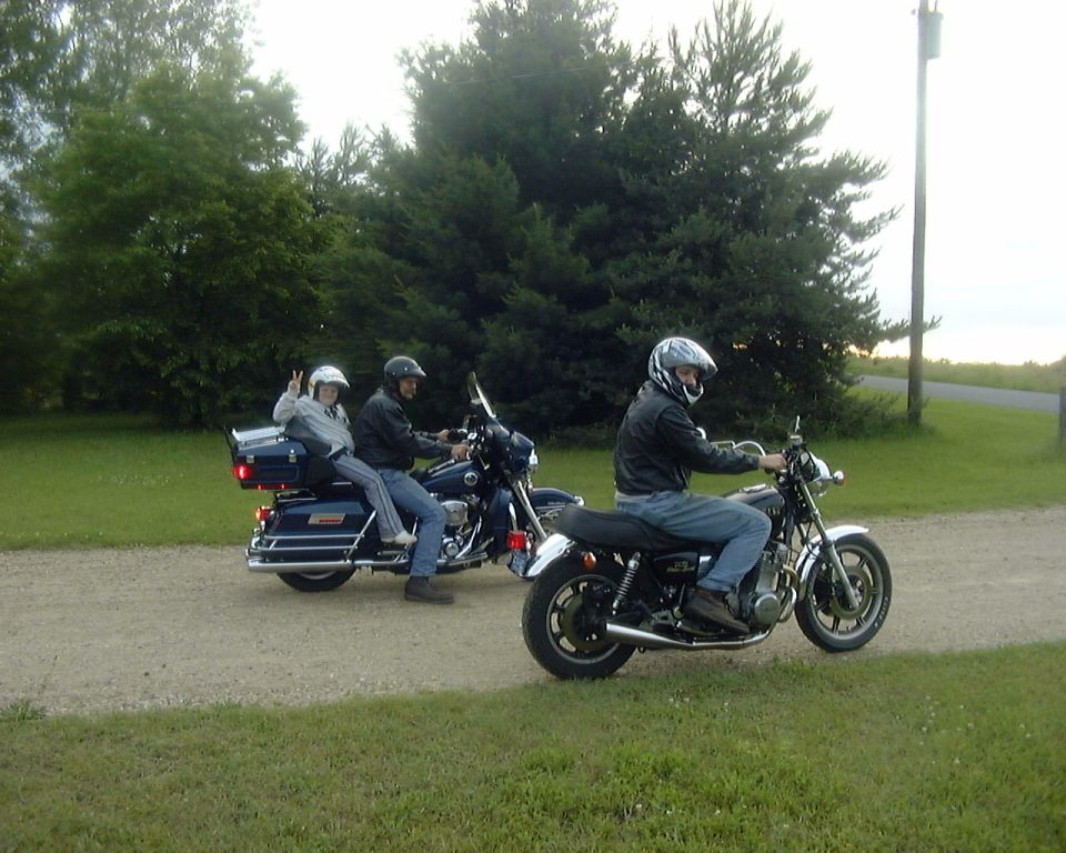Two riders on a blue full-dress touring motorcycle and a black cruiser on a gravel driveway