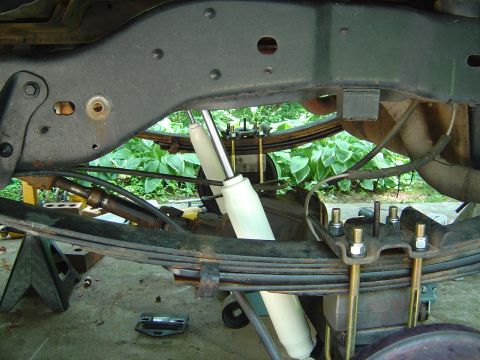 1986 Ford Bronco - Underside view of a rear leaf-spring suspension showing a new white shock absorber mounted vertically, U-bolts securing the axle to the lea…