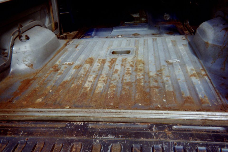 Bare rusty blue ribbed cargo floor pan inside a stripped Bronco, viewed from the open tailgate