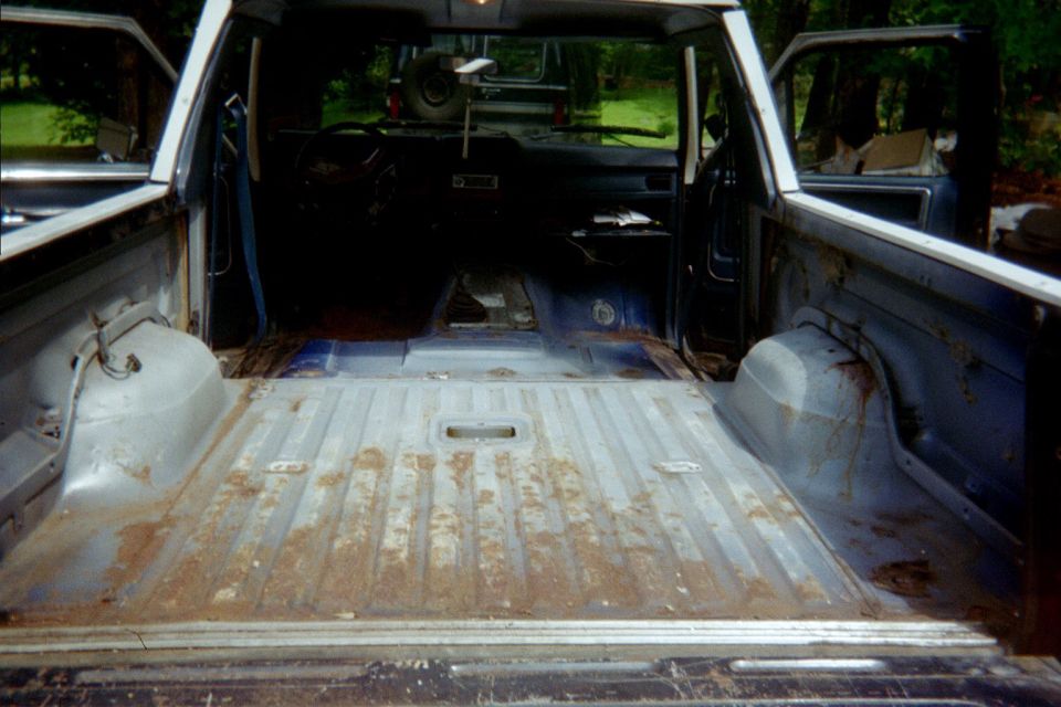 Stripped interior of blue Ford Bronco seen from rear, bare rusty metal floor, seats removed