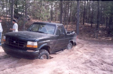 1995 Ford Bronco - A black 1995 Ford Bronco is stuck in the sand with two people standing nearby.
