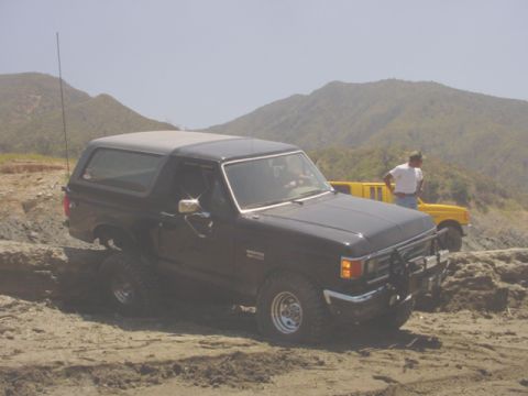 1988 Ford Bronco - 1988 Ford Bronco navigating a sandy, off-road course with another vehicle in the background.