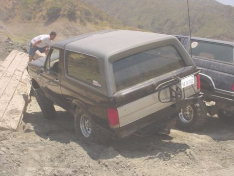 1988 Ford Bronco - A man watches a 1988 Ford Bronco navigate a rough terrain with another vehicle behind it.
