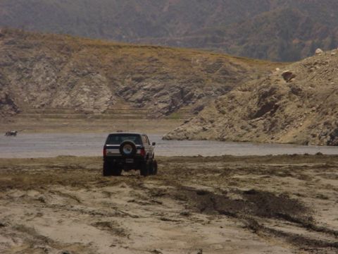 1988 Ford Bronco - A dark SUV navigates a dry, dusty terrain near a body of water.