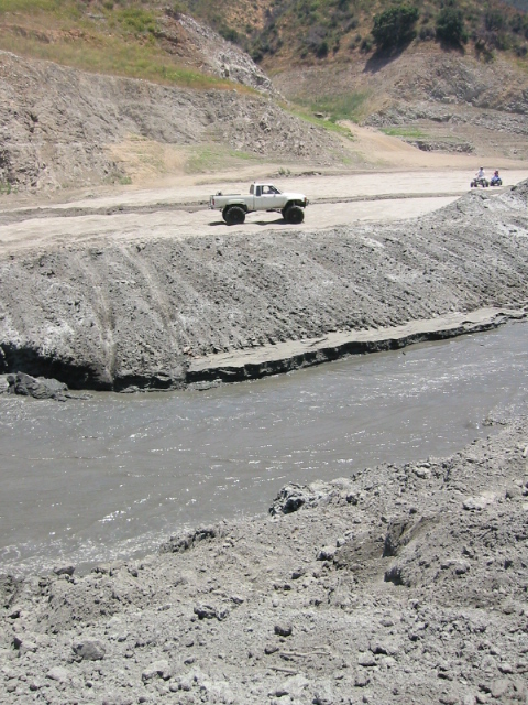 1985 Ford Bronco - A white pickup truck navigates a muddy terrain with another vehicle visible in the distance.