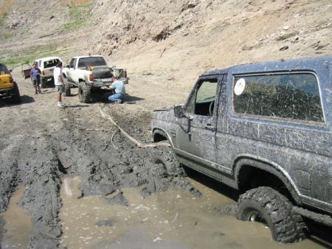 1985 Ford Bronco - Several vehicles are stuck in deep mud on an off-road trail.