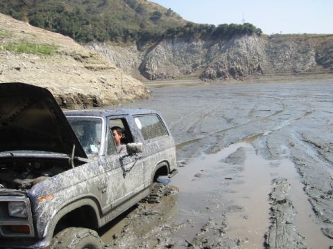 1985 Ford Bronco - This SUV is stuck deep in the mud with its hood up, suggesting mechanical trouble in a desolate, dry lakebed.