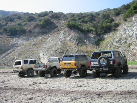 1985 Ford Bronco - Several off-road vehicles are lined up in a dry, rocky landscape.