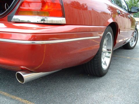 1999 Ford Crown Victoria - The rear of a red sedan is visible, showing its chrome trim and exhaust pipe.