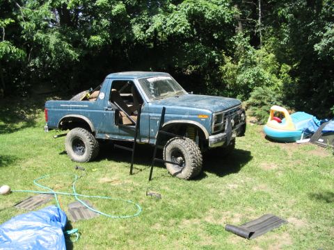 1986 Ford Bronco - Modified blue pickup truck sits in a grassy yard with trees in the background.