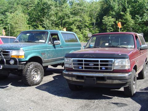 1993 Ford Bronco - Two Ford Broncos are parked outdoors, with trees in the background and a gravel lot in the foreground.