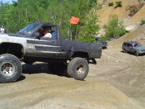 1993 Ford Bronco - Multiple off-road vehicles navigate a dusty, hilly terrain with trees in the background.