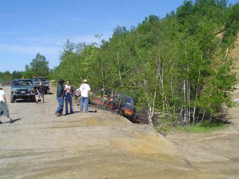 1993 Ford Bronco - People gather around vehicles on a dirt track, with one SUV tilted precariously on a slope.