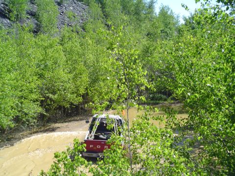 1993 Ford Bronco - A red pickup truck navigates a muddy terrain surrounded by lush green foliage.