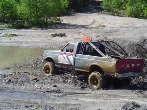1993 Ford Bronco - A modified Ford pickup truck is stuck in the mud with a branch across its front tire.