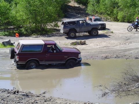 1993 Ford Bronco - A maroon 1993 Ford Bronco navigates a muddy obstacle course, with other vehicles visible in the background.