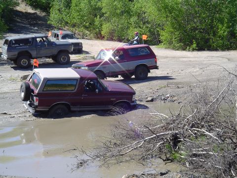 1993 Ford Bronco - Multiple Ford Broncos navigating a muddy off-road course on a sunny day.