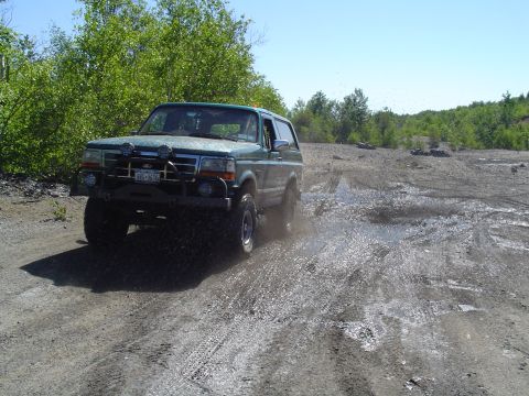 1993 Ford Bronco - This Ford Bronco is navigating a muddy off-road course with trees in the background.