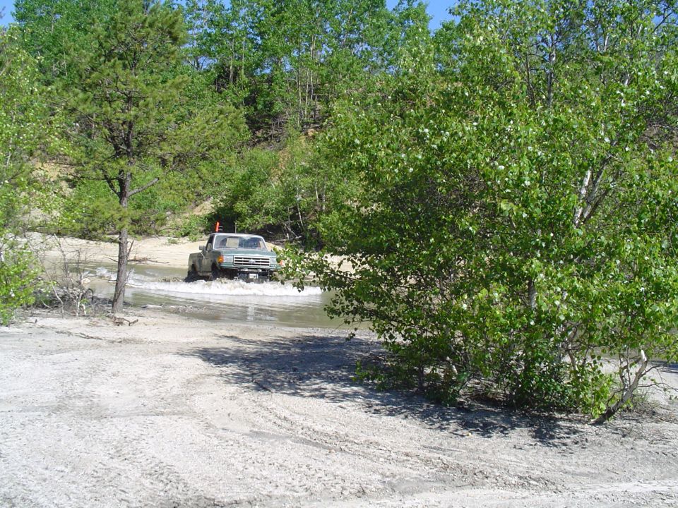 Light-colored pickup truck driving through water, off-road scene
