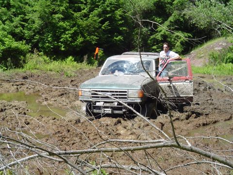 1993 Ford Bronco - A 1993 Ford Bronco is stuck in a muddy area with trees in the background.
