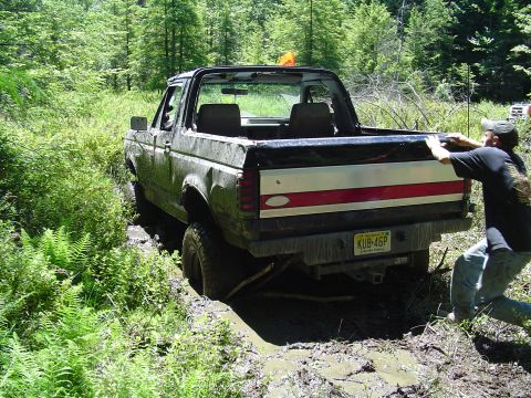 1993 Ford Bronco - A person attempts to push a 1993 Ford Bronco out of a muddy trail.