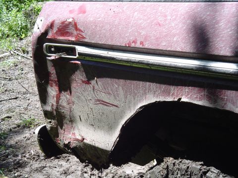1993 Ford Bronco - The rear quarter panel of a red SUV shows significant damage and is covered in mud.