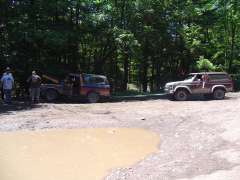 1993 Ford Bronco - Two Ford Bronco SUVs are parked on a dirt road, with one having its hood open and the other in the background.