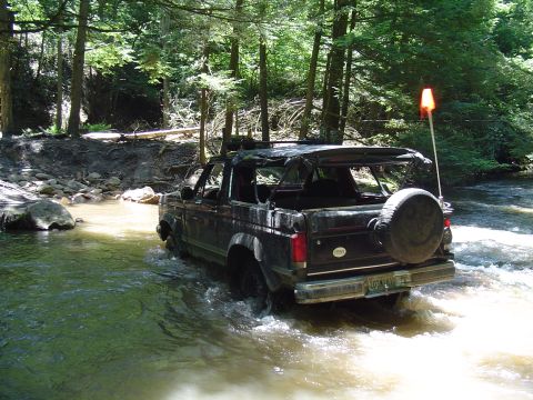 1993 Ford Bronco - This 1993 Ford Bronco navigates a rocky stream bed surrounded by lush green trees.