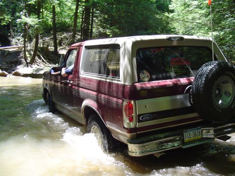 1993 Ford Bronco - A Ford Bronco navigates a wooded stream, kicking up water as it goes.
