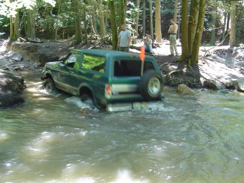 1993 Ford Bronco - This SUV is navigating a water obstacle in a forest setting.
