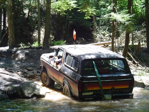 1993 Ford Bronco - This Ford Bronco is navigating a rocky stream bed in a forest, with its rear end submerged in water.