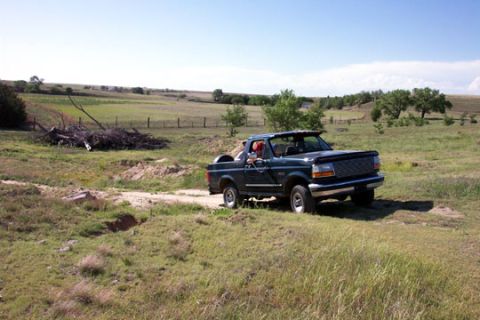 1995 Ford Bronco - Dark green 1995 Ford Bronco navigates a rural dirt road under a clear blue sky.