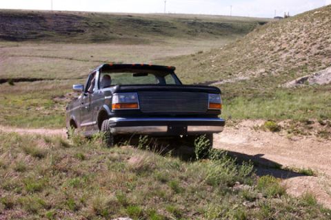 1995 Ford Bronco - A 1995 Ford Bronco navigates a dirt path through a grassy, hilly landscape.